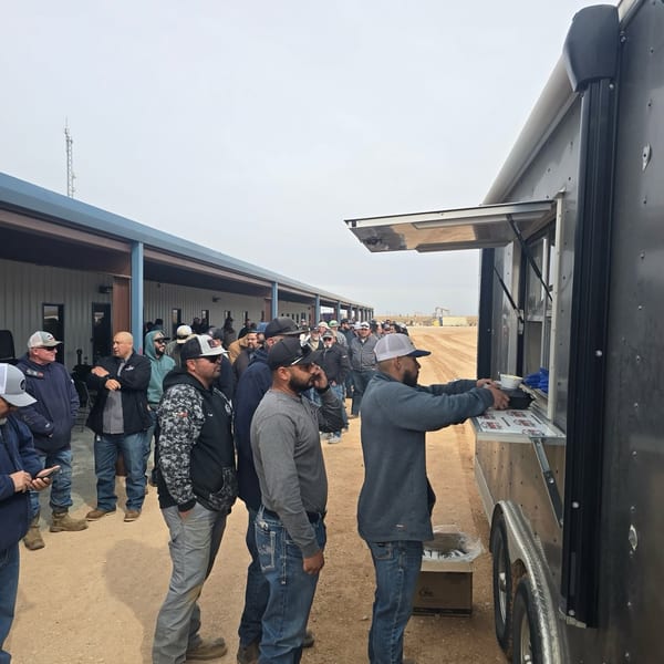 A long line of men in work clothes wait to receive food from a food truck.